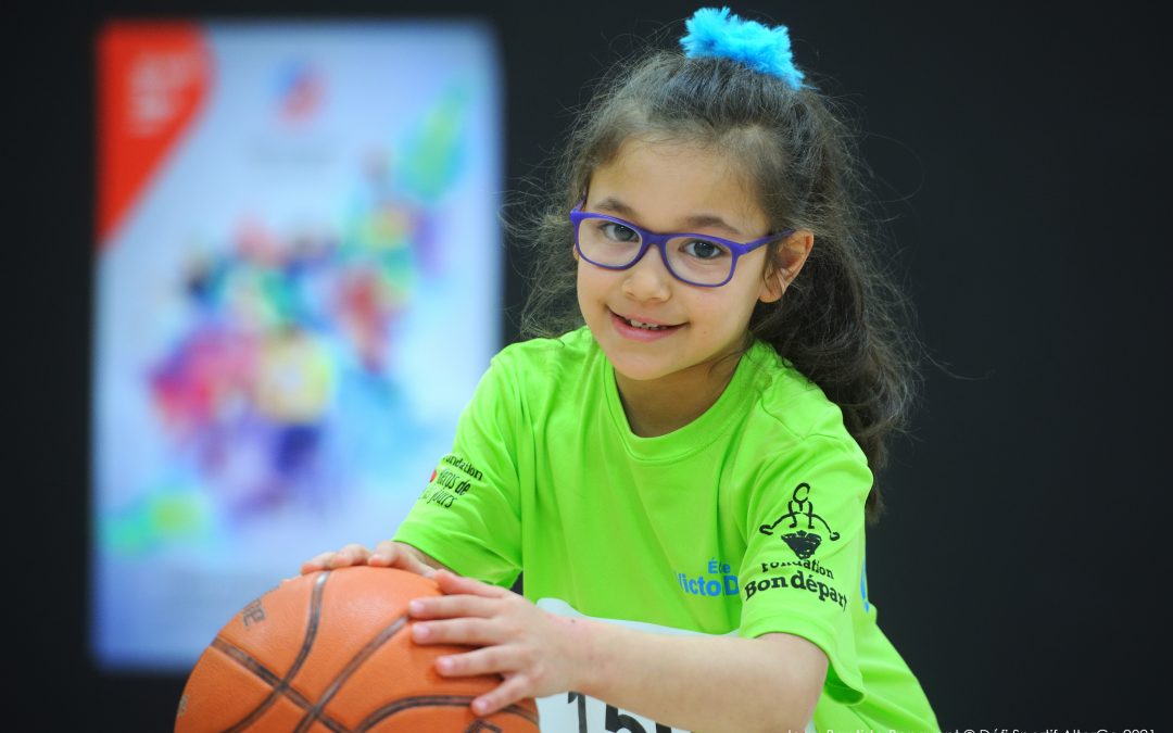 Une petite fille drible avec un ballon de basketball en regardant la caméra.