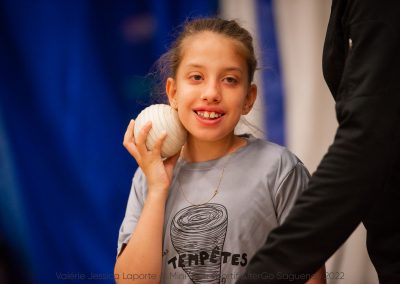 Une jeune fille souriante tient une balle au niveau de sa joue.