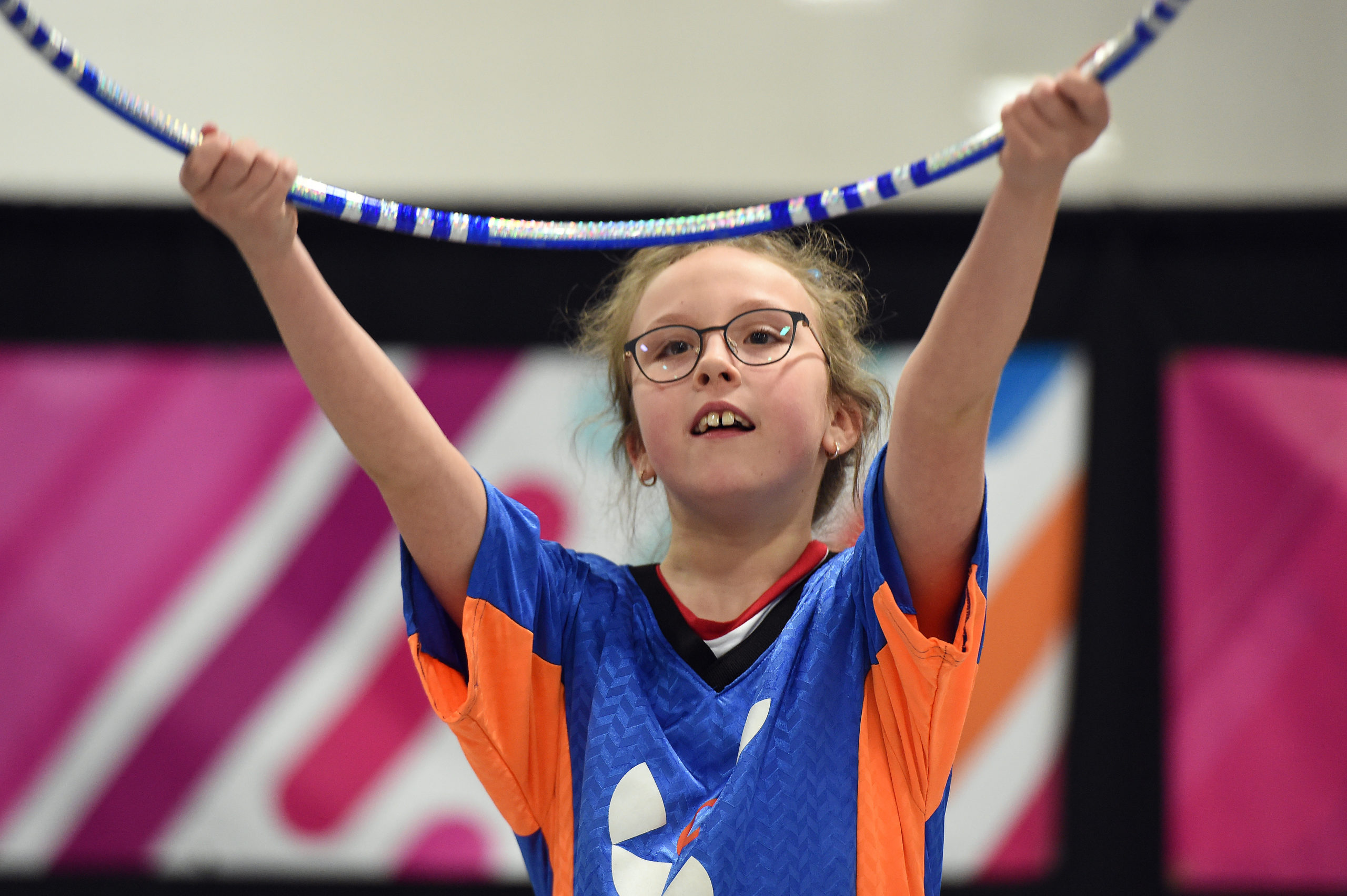 Une jeune fille tient un cerceau à bout de bras pendant sa routine de gymnastique rythmique.