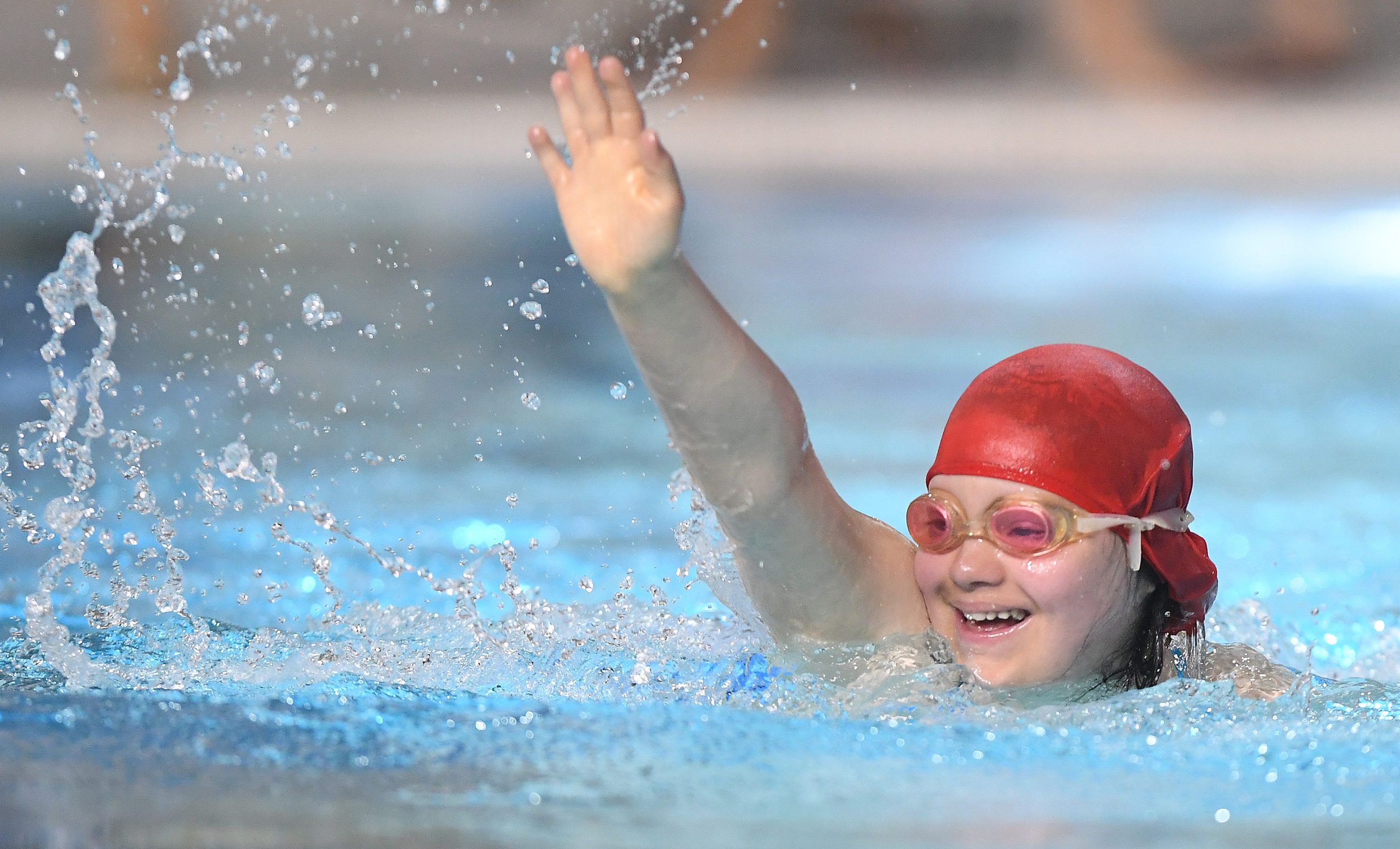 Une athlète en natation sourit et tend un bras vers le ciel.