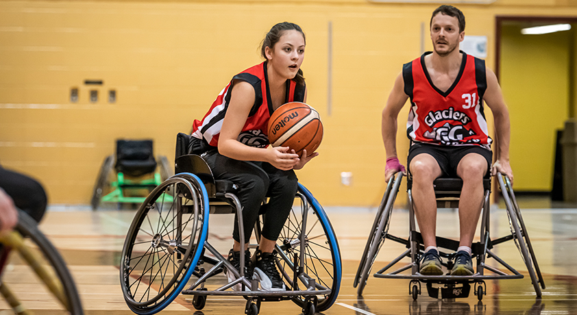 Une fille en fauteuil roulant tenant un ballon de basketball lors d'un match.