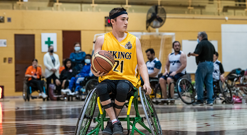 Un joueur en fauteuil roulant tient un ballon de basketball.