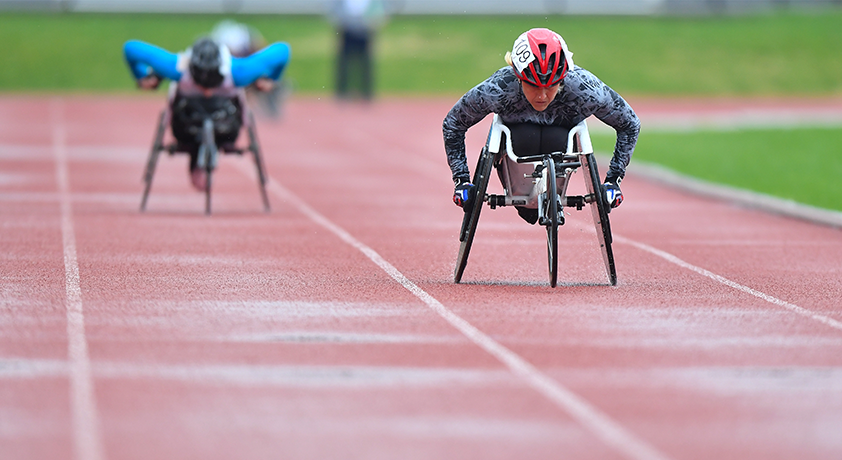 Deux personnes en fauteuil roulant roulent sur une piste d'athlétisme.