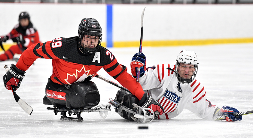 Un joueur de parahockey de l'équipe Canada et un joueur de l'équipe des États-Unis foncent vers la rondelle.