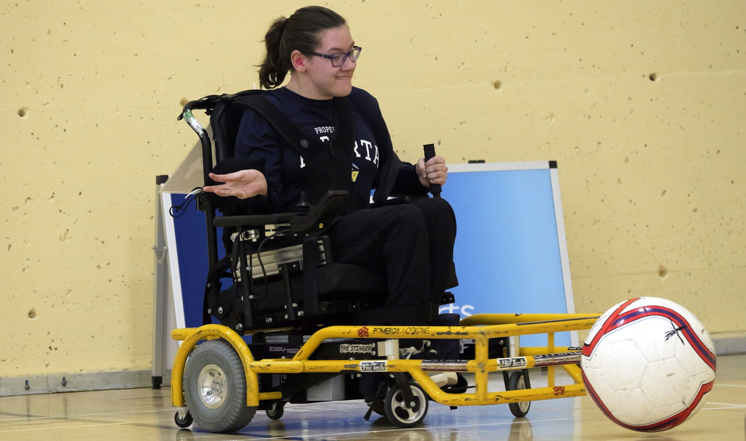 Une athlète en fauteuil roulant en action pendant un match de powerchair soccer.