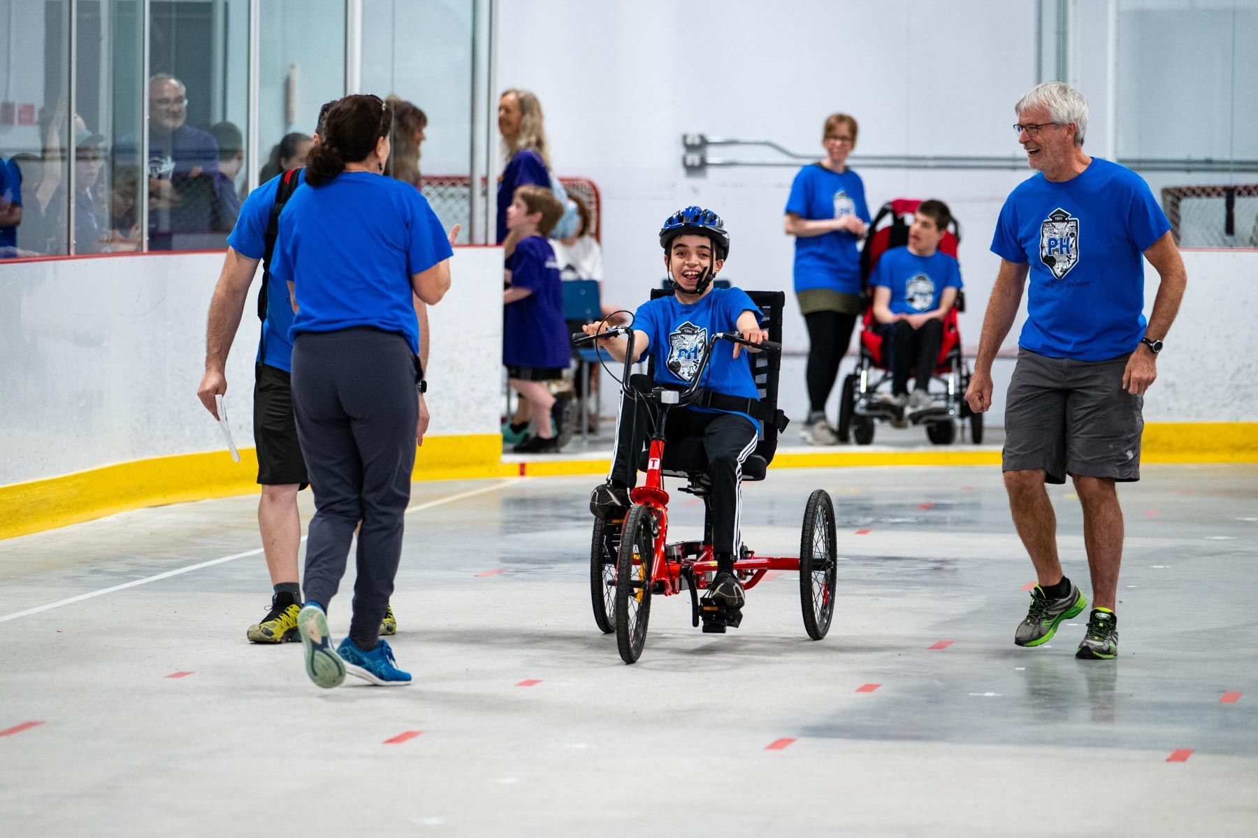 3 adultes encouragent un jeune garçon souriant en tricycle.