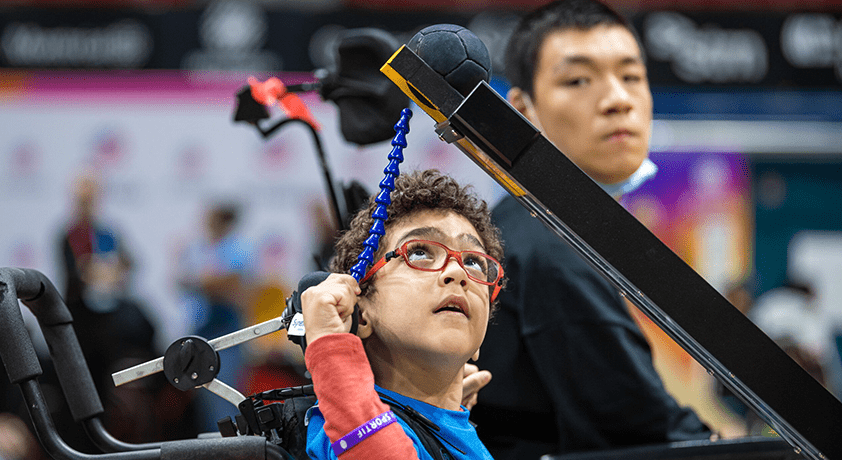 Un garçon pousse une balle de boccia à l'aide d'une baguette.