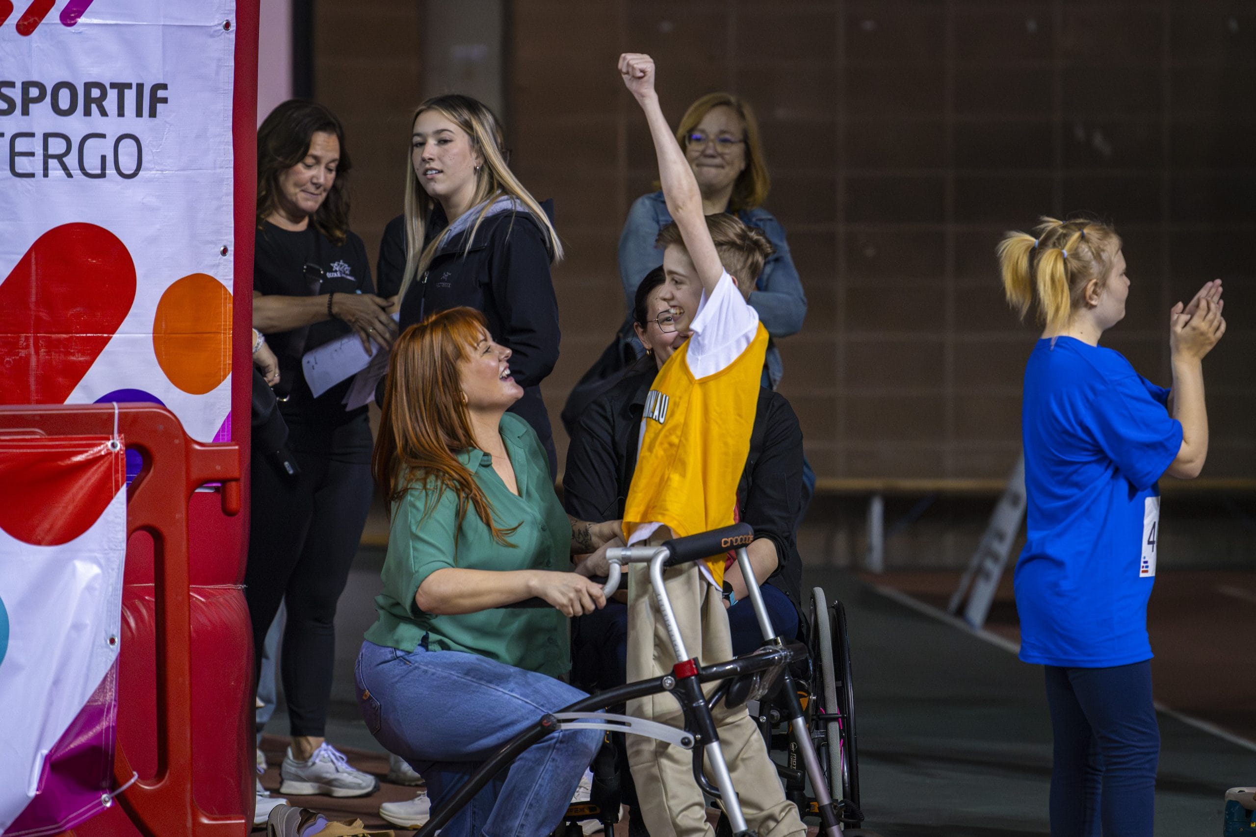 Un athlète lève un bras en l'air avec sa mère qui le regarde avec fierté.