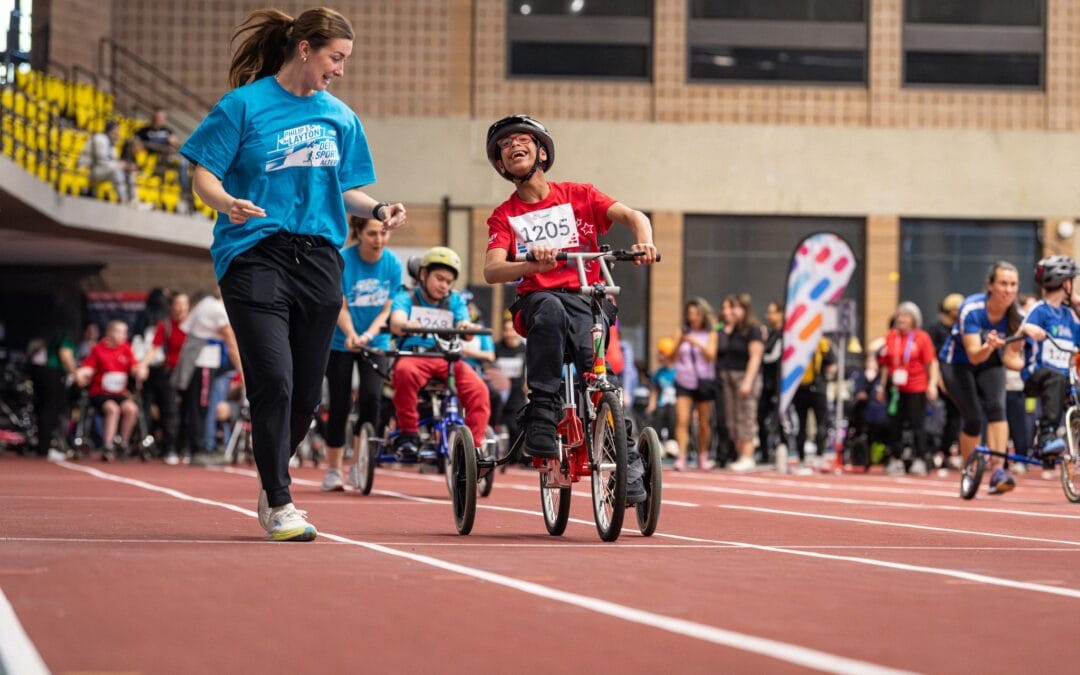 Un jeune du volet scolaire prend part à la course en tricycle, encouragé par son enseignante